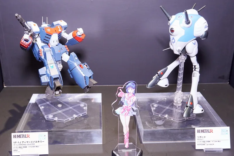 こちらは歴代マクロスシリーズの歴史をテーマにした展示エリア。「HI-METAL R」や「DX超合金」の新規造形も多数含む歴代バルキリーとともに、これも新アイテムの「アクリルスタンドキーホルダー」で歴代の歌姫たち（＆熱気バサラ）が並びました。
「HI-METAL R」では「VF-4 ライトニングIII」「VF-2SS バルキリーII」「VF-0A フェニックス」、「DX超合金」の「YF-19」「VF-19改エクスカリバー 熱気バサラスペシャル」と、参考出品もファン待望の機体揃い。